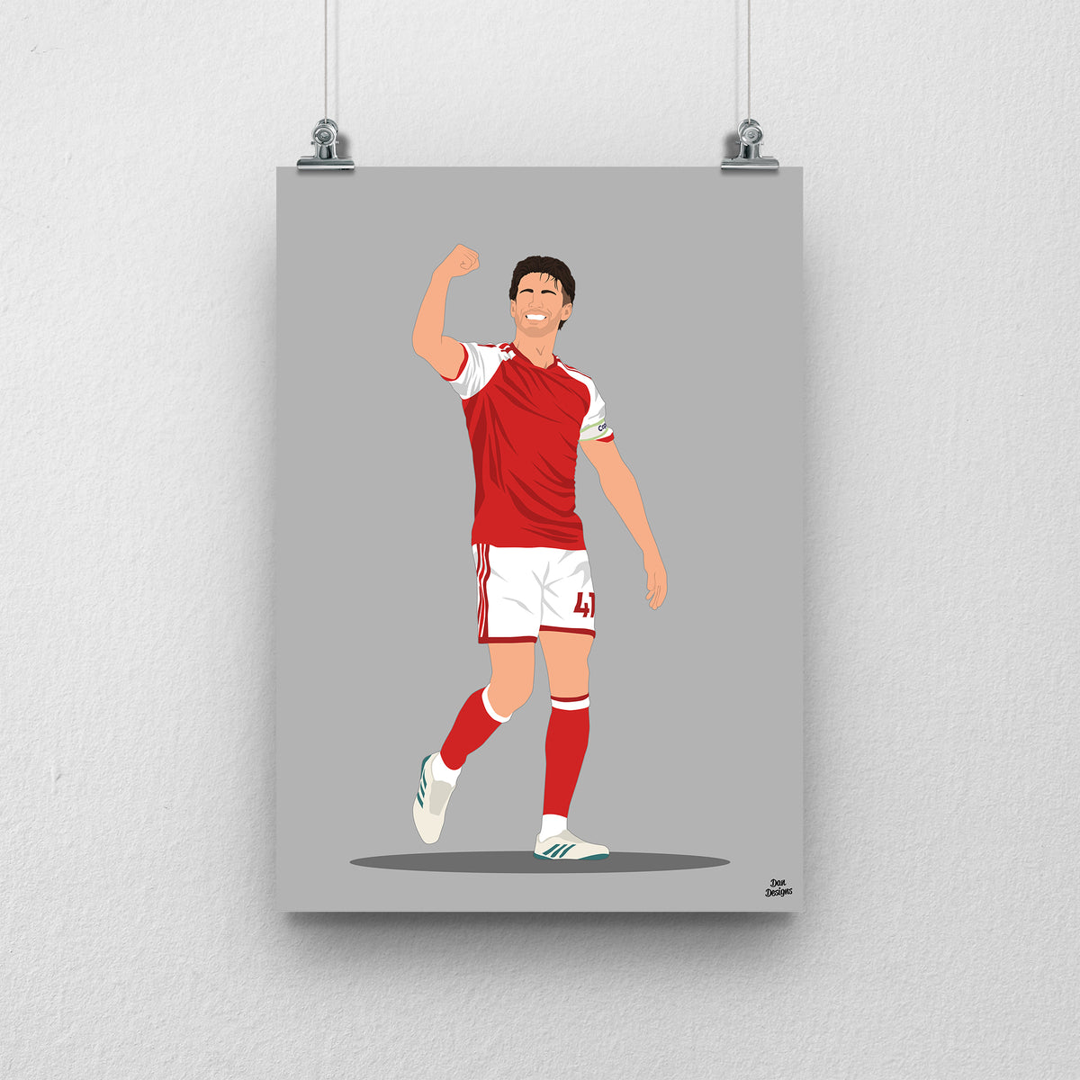 Declan Rice in Arsenal's red-and-white kit, celebrating with one arm raised and bent, against a grey background.