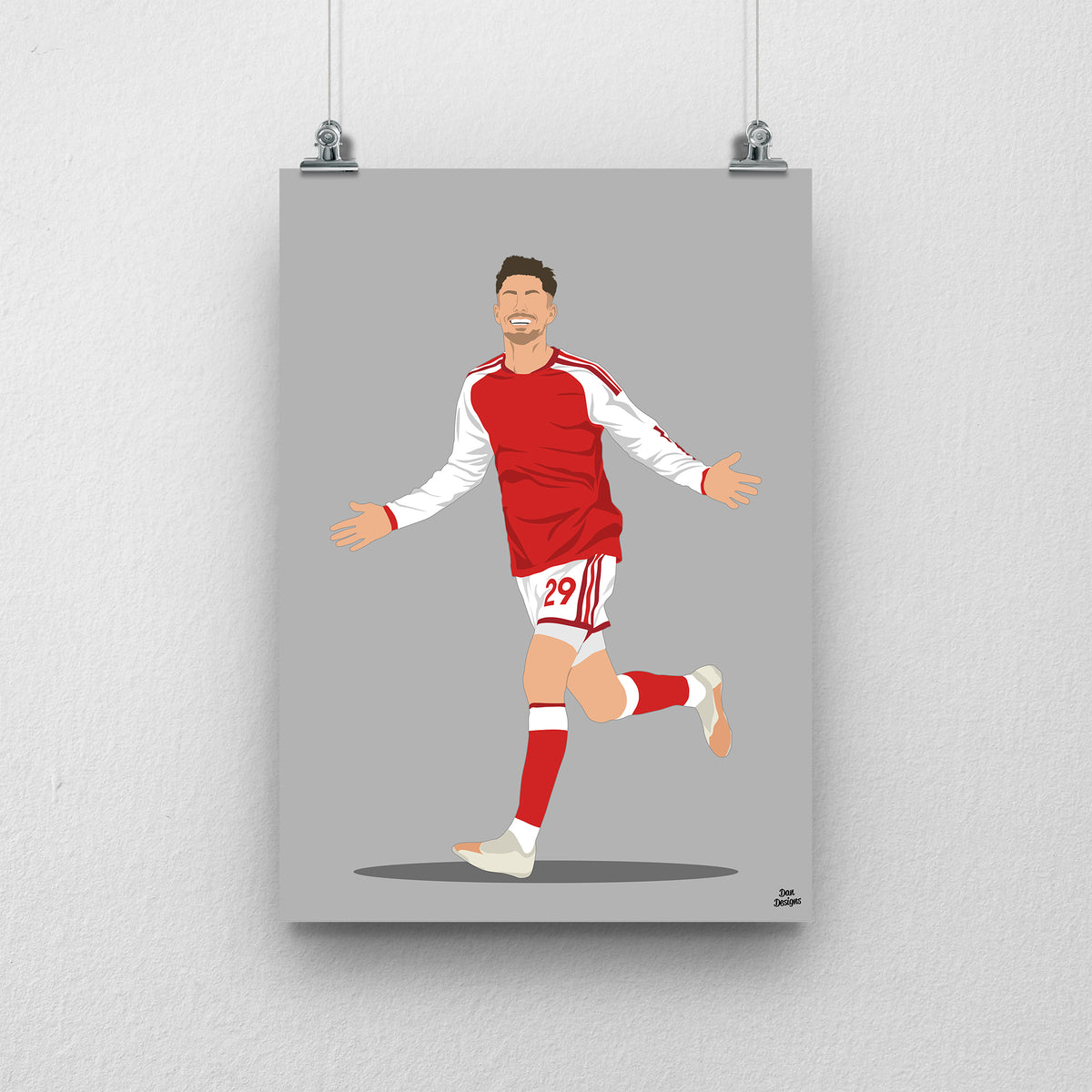 Kai Havertz running with both arms out in Arsenal's red shirt with white sleeves, against a grey background.