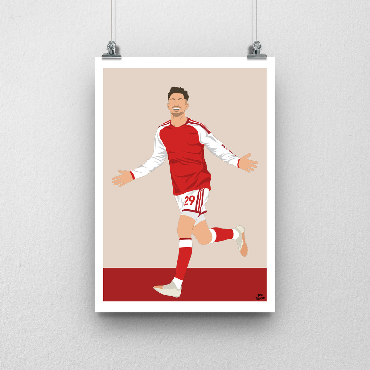 Kai Havertz running with both arms out in Arsenal's red shirt with white sleeves, against a beige background with a white border and red base.