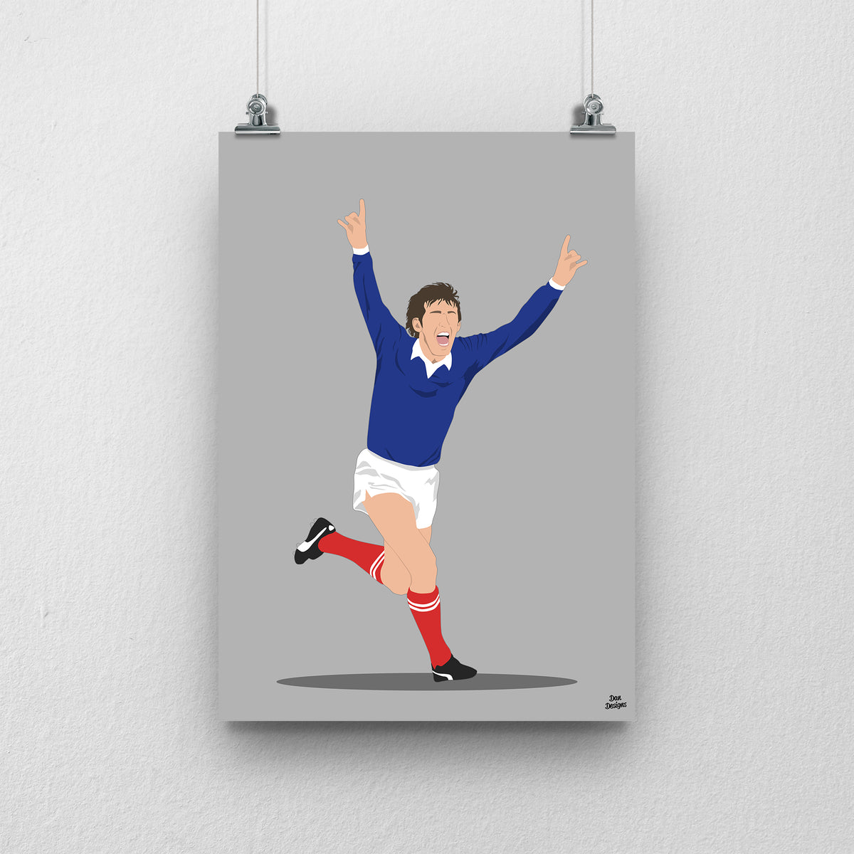 Kenny Dalglish celebrating with both arms raised in Scotland’s navy shirt, white shorts and red socks, illustrated with a grey background.